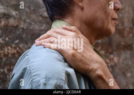 Schmerzen im Schultermuskel des südostasiatischen älteren Mannes. Konzept der Nackensteifigkeit. Stockfoto