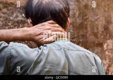 Schmerzen im Nackenmuskel des südostasiatischen älteren Mannes. Konzept von Nackenschmerzen und Nackensteifigkeit. Stockfoto