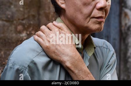 Schmerzen im Schultermuskel des südostasiatischen älteren Mannes. Konzept der Nackensteifigkeit. Stockfoto