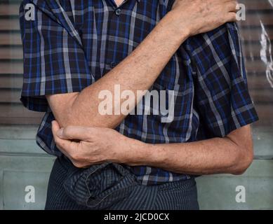 Schmerzen im Ellenbogengelenk des südostasiatischen älteren Mannes. Konzept von Ellenbogenschmerzen, rheumatoider Arthritis und Armproblemen. Stockfoto