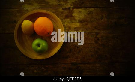 Auf einem Holztisch steht eine Obstplatte. Apfel, Zitrone und Orange. Blick von oben Stockfoto
