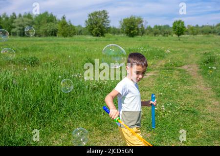 Vorschulkinder blasen an einem sonnigen Tag große Seifenblasen auf einem Feld Stockfoto