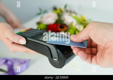 Nahaufnahme der Hände einer Kundin, die am Bankzahlungsterminal Blumen mit Kreditkarte kauft. NFC-Technologie. Stockfoto