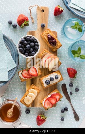 Frühstückscracker mit verschiedenen frischen Früchten und Frischkäse oder Nussbutter. Stockfoto
