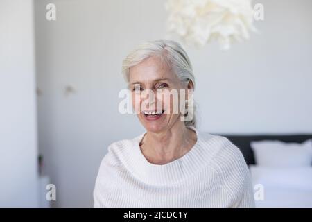 Porträt einer kaukasischen älteren Frau, die lächelt und zu Hause auf dem Bett sitzt Stockfoto