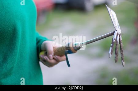 Kaukasische Gärtnerin im Garten zeigt einen Rechen. Das Konzept von Gartenarbeit und nachhaltigem Sommer. Die Hand der Frau mit einem Gartenwerkzeug. Häckslerrechen für Stockfoto