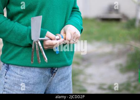 Kaukasische Gärtnerin im Garten zeigt einen Rechen. Das Konzept von Gartenarbeit und nachhaltigem Sommer. Die Hand der Frau mit einem Gartenwerkzeug. Häckslerrechen für Stockfoto