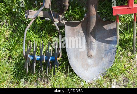 Gartengeräte. Gartengeräte auf dem Hintergrund eines Gartens in grünem Gras. Sommerarbeitswerkzeug. Schaufel, Gabel und Backpulver im Garten gestapelt Stockfoto