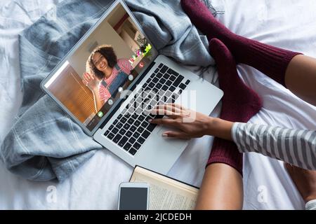 Unterer Teil der kaukasischen Frau, die Socken trägt, Videokonferenzen über dem Laptop, während sie sich auf dem Bett entspannt Stockfoto