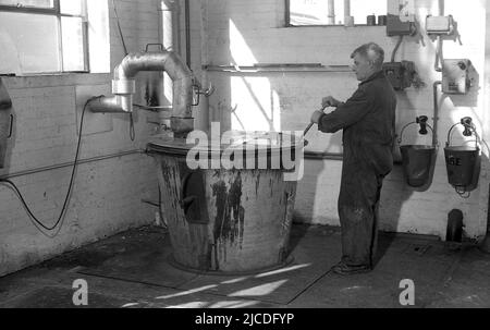 1960s, historisch, in einer Ecke einer Lackierfabrik, ein männlicher Betrieb, der einen Stahlstab verwendet, um Farbe in einem großen Metallmischbehälter oder -Eimer zu mischen, England, Großbritannien. In dieser Zeit in Großbritannien gab es über 1.000 kleine Unternehmen, die Farben und Spezialbeschichtungen herstellten, aber im Laufe der Zeit wurde diese Zahl bis zur Jahrhundertwende auf weniger als fünfzig reduziert. Stockfoto