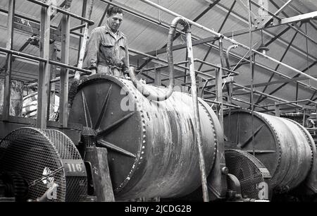 1960s, historisch, in einer Lackierfabrik, ein männlicher Arbeiter in Overalls, der über Maschinen auf dem Fabrikboden stand, England, Großbritannien. In dieser Zeit in Großbritannien gab es über 1.000 kleine Unternehmen, die Farbe herstellten, aber im Laufe der Zeit wurde diese Zahl bis zur Jahrhundertwende auf weniger als fünfzig reduziert. Stockfoto