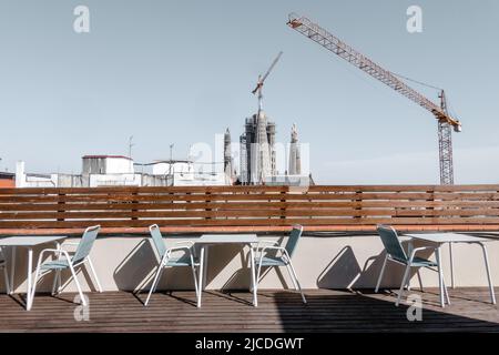 Barcelona, Spanien - 29. Mai 2022: Tische und Stühle auf einer Terrasse. Im Hintergrund sieht man Kraniche und die Türme der Basilika Stockfoto