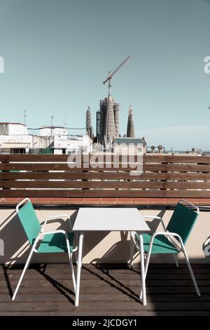Barcelona, Spanien - 29. Mai 2022: Tische und Stühle auf einer Terrasse. Im Hintergrund sieht man Kraniche und die Türme der Basilika Stockfoto