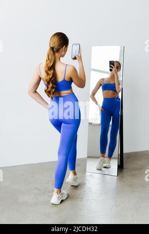 Portrait einer stolzen muskulösen Frau mit ihrer fittenden Figur und ihrer schlanken Taille, die nach dem Training in einem Sportspiegel fie macht und posiert Stockfoto