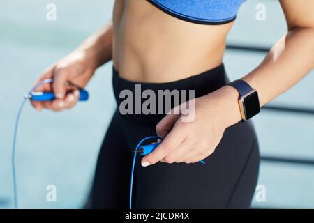 Nahaufnahme einer nicht erkennbaren Frau mit Fitness-Tracker mit Springseil für das Ausdauertraining im Freien Stockfoto