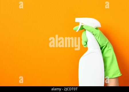 Desinfektionsmittel-Sprühflasche Mockup in weiblicher Hand in grünem Gummihandschuh über orangefarbenem Hintergrund. Küchenreiniger Produktdesign. Stockfoto