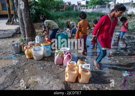 Slum-Kinder füllen ihre Behälter mit Wasser aus einer Wasserleitung am Straßenrand in Ghaziabad. Slum Kinder sammeln Trinkwasser und nutzen täglich Wasser aus einer Wasserleitung am Straßenrand. Stockfoto