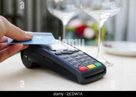 Zahlungsterminal mit Kreditkarte in der Nähe von Gläsern und Tellern auf dem Tisch im Restaurant. Konzept der elektronischen Finanzierung. Stockfoto