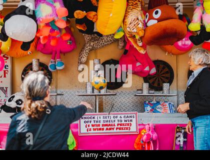 Frau in schwarzem Mantel, die beim Morpeth Fair Day, 2022. Juni, Northumberland, einen Ball auf Blechdosen wirft Stockfoto