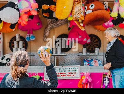 Frau in schwarzem Mantel, die beim Morpeth Fair Day, 2022. Juni, Northumberland, einen Ball auf Blechdosen wirft Stockfoto