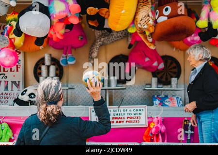 Frau in schwarzem Mantel, die beim Morpeth Fair Day, 2022. Juni, Northumberland, einen Ball auf Blechdosen wirft Stockfoto