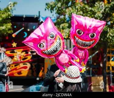 Die Rückansicht einer Person, die einen Hut mit zwei leuchtend rosa Katzenballons trägt, Morpeth Fair Day, 2022. Juni, Northumberland Stockfoto