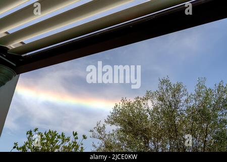 Bunte schillernde Wolke, wunderschöne Regenbogenwolke über oliver-Bäumen und Pergola La Rochelle Frankreich Stockfoto