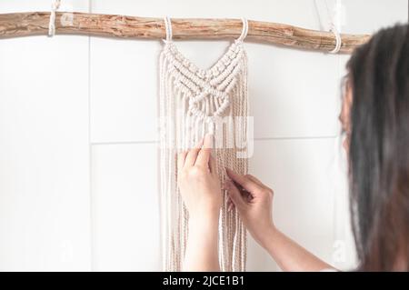 Mädchen webt ein Makrammuster aus natürlichen weißen Baumwollfäden für eine große Wandverkleidung Stockfoto