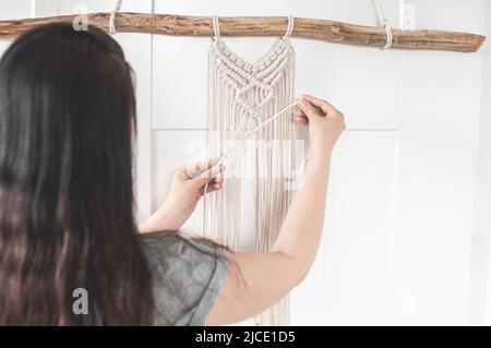 Mädchen webt ein Makrammuster aus natürlichen weißen Baumwollfäden für eine große Wandverkleidung Stockfoto