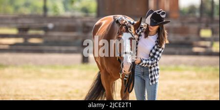 Die junge Frau legt draußen einen Zaum auf den Kopf des Pferdes. Stockfoto