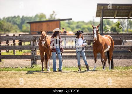 Zwei junge Cowgirls gehen im Sommer mit ihren Malpferden auf einer Ranch.