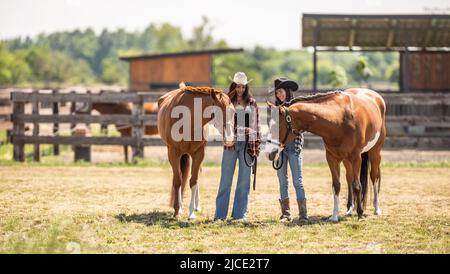 Zwei Cowgirls treffen ihre Malpferde an einem sonnigen Tag auf einer Ranch.