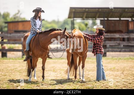 Zwei Freundinnen auf einer Ranch bereiten sich auf einen Pferderitt vor.