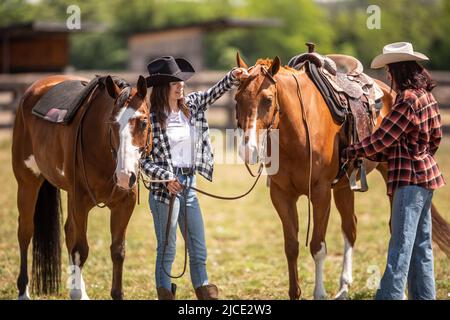 Cowgirl fixiert einen Sattel auf einem Malpferd, während ihr Freund hilft, ihr Pferd zu halten. Stockfoto