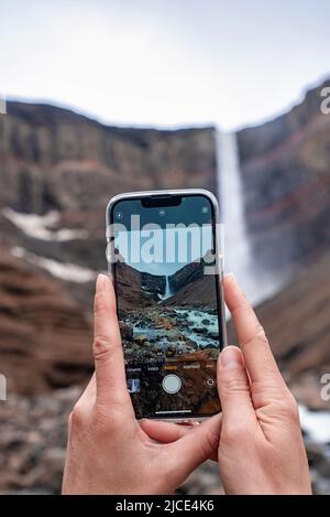 Zugeschnittenes Bild eines Touristen, der den Wasserfall von Hengifoss über ein Smartphone fotografiert Stockfoto