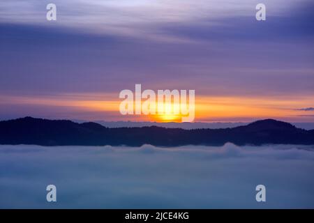 Neblige Wolken fielen bei Sonnenaufgang unter die Berghöhe, oranger und violetter Horizont, Ukraine Stockfoto