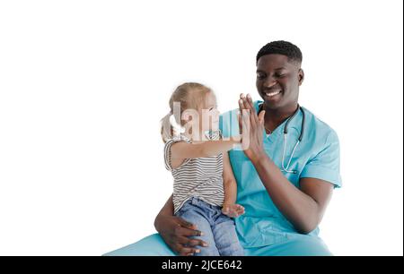 Ein afroamerikanischer Kinderarzt hält ein kleines glückliches Mädchen auf dem Schoß, lacht und klatscht mit den Händen. Familienarzt Stockfoto