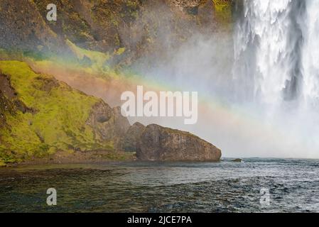 Schöner Regenbogen über Felsformationen und Skoga Fluss gegen Skogafoss Stockfoto