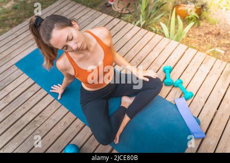 Fokussierte junge Frau in Sportkleidung, die ihren Hals streckt, während sie draußen auf der Matte arbeitet. Stockfoto