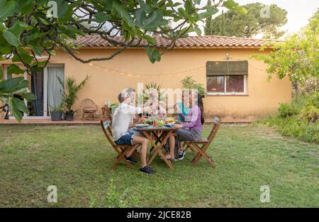 Glückliche Freunde essen und Verkostung zusammen im Garten in Grill Dinner-Party im Sommer. Lächelnde Menschen essen auf der Terrasse des Hauses. Lächeln, Fröhlichkeit Stockfoto
