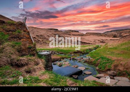 Turf House und geothermische Quelle in Hrunalaug gegen dramatischen Himmel während des Sonnenuntergangs Stockfoto