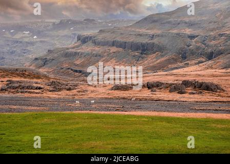 Malerische Aussicht auf grasbewachsenen Feld gegen majestätische Berge im Tal während des Sonnenuntergangs Stockfoto