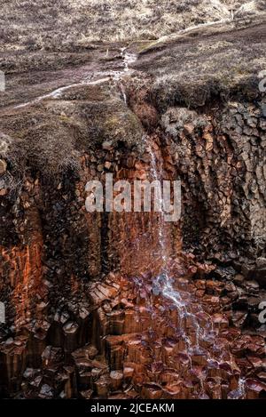 Wunderschöne Aussicht auf einen kleinen Wasserfall, der vom Berg über Basaltsteinsäulen fällt Stockfoto