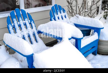 Zwei blaue Adrirondack-Stühle in einem von Schnee bedeckten Hinterhof Stockfoto