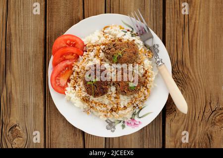 Drei Linsen-Hacksteaks mit Reis, Mikrogemüse und Tomate in weißer Platte auf Holzhintergrund horizontal Stockfoto