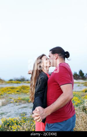 Porträt eines hübschen Paares mittleren Alters, das sich küsst und umarmt, während es im Sommerpark auf Gras steht. Stockfoto