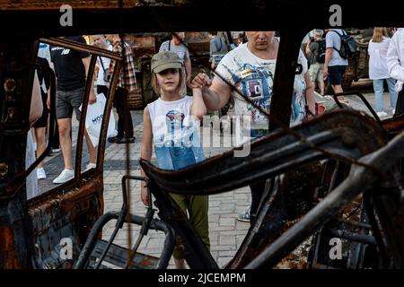 Kiew, Ukraine. 12.. Juni 2022. Ein Mädchen schaut auf ein verbranntes Auto während einer Ausstellung zerstörter ukrainischer Bürgerwagen und russischer Kriegsfahrzeuge, die auf dem Michailovskyi-Platz in der Altstadt von Kiew ausgestellt wurden. Als die Russische Föderation vor 3 und einem halben Monat in die Ukraine einmarschierte, dauern die heftigen Kämpfe im Osten des Landes an. Die Hauptstadt Kiew bleibt in relativer Sicherheit, obwohl in der ganzen Stadt Erinnerungen an den Krieg wie schützende Sandsäcke, Straßensperren, nationale und Antikriegszeichen zu sehen sind. Kredit: SOPA Images Limited/Alamy Live Nachrichten Stockfoto