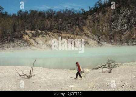 Eine Frau, die auf einer sandigen Landschaft auf dem Krater des Mount Patuha, der im Volksmund als Kawah Putih (weißer Krater) in Ciwidey, Bandung, West Java, Indonesien, bekannt ist, spazieren geht. Stockfoto