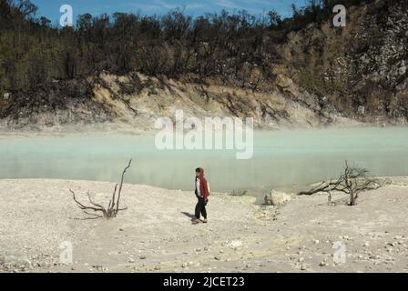 Eine Frau, die auf einer sandigen Landschaft auf dem Krater des Mount Patuha, der im Volksmund als Kawah Putih (weißer Krater) in Ciwidey, Bandung, West Java, Indonesien, bekannt ist, spazieren geht. Stockfoto