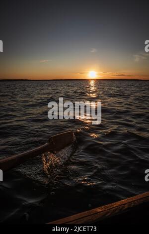 Planschen Sie während des Sonnenuntergangs vom Ruderboot auf dem Boot auf einem See Stockfoto